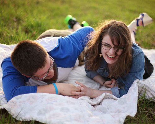 A Couple Laying Down on a Picnic Blanket Smiling and Holding Hands 